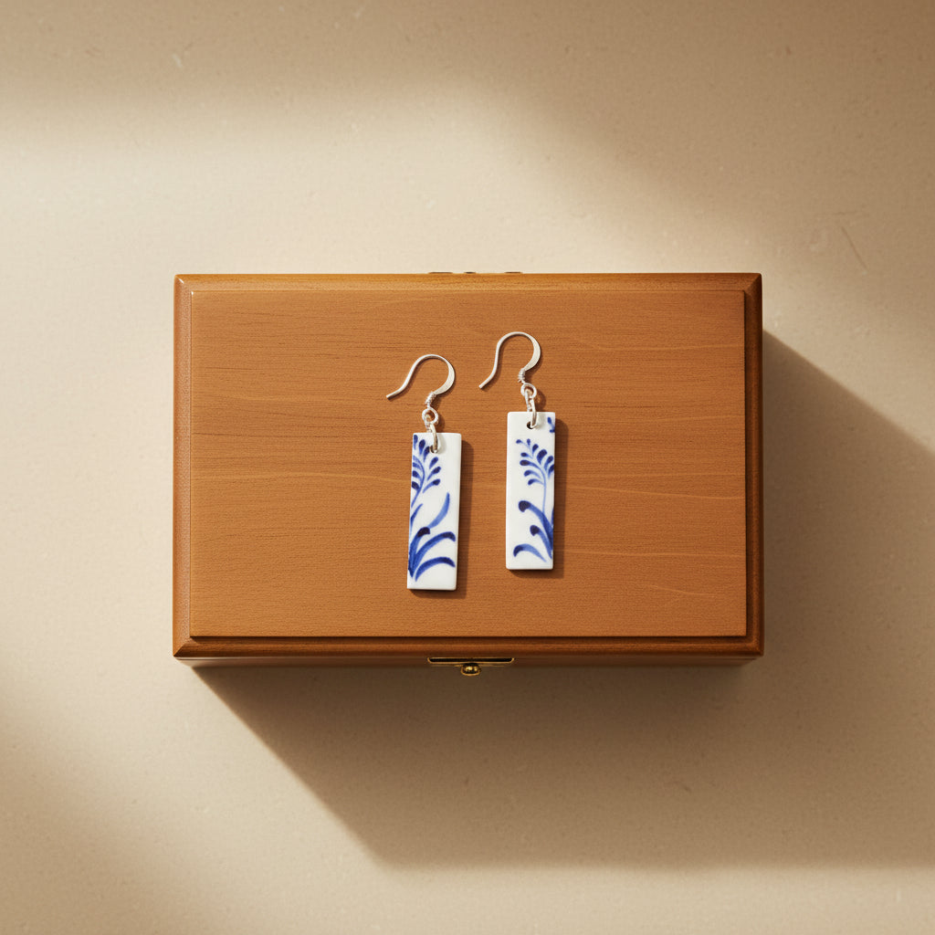 Pair of earrings with blue floral patterns on a wooden box with a light beige background