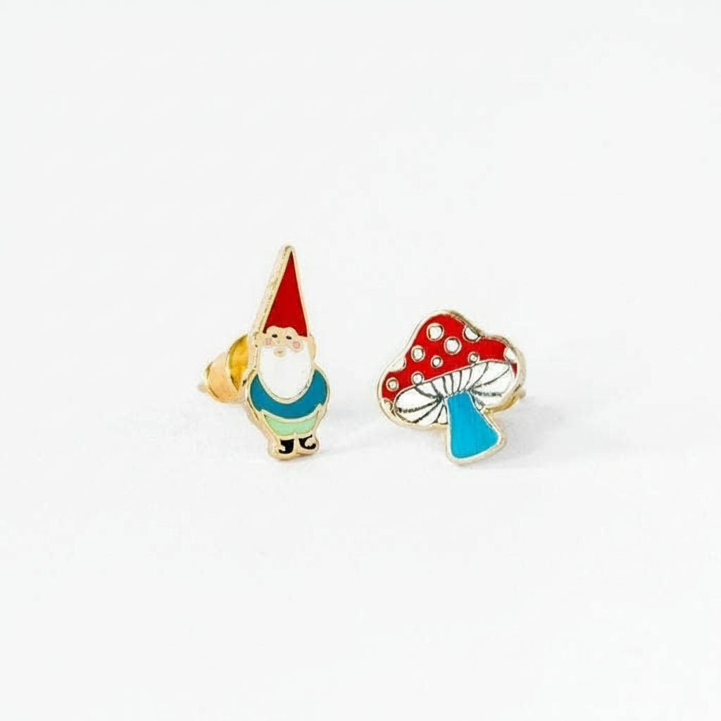 A pair of gold stud earrings, one featuring a gnome and the other a mushroom, both with enamel detailing.