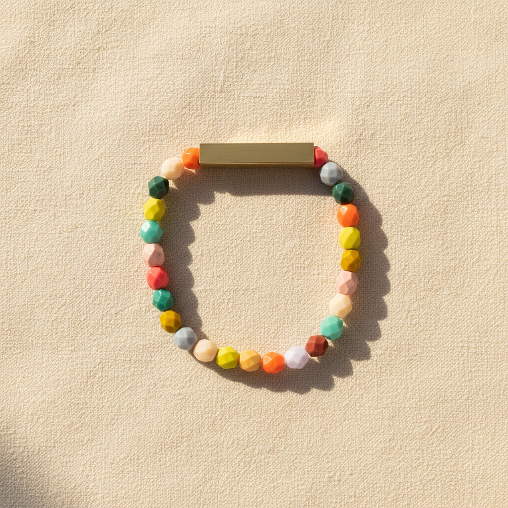 A colorful beaded bracelet with brass accents displayed on a textured beige background