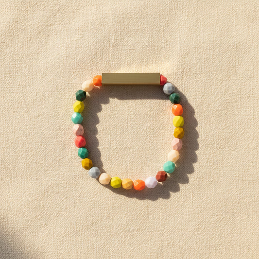 A colorful beaded bracelet with brass accents displayed on a textured beige background