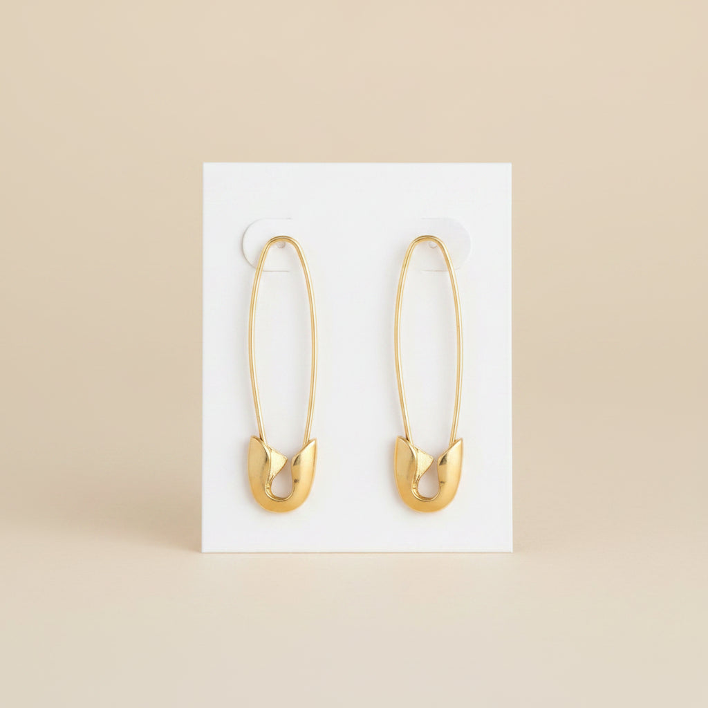 Gold safety pin earrings on a white backing card and a beige background