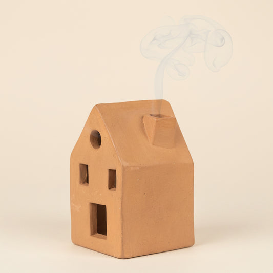 Terracotta incense holder shaped like a home with incense smoke comes from the chimney with a white background