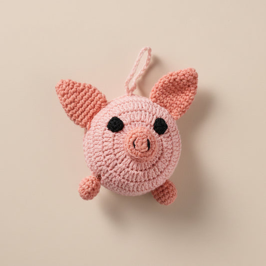 Close up of the crocheted pink pig tape measure on a concrete surface