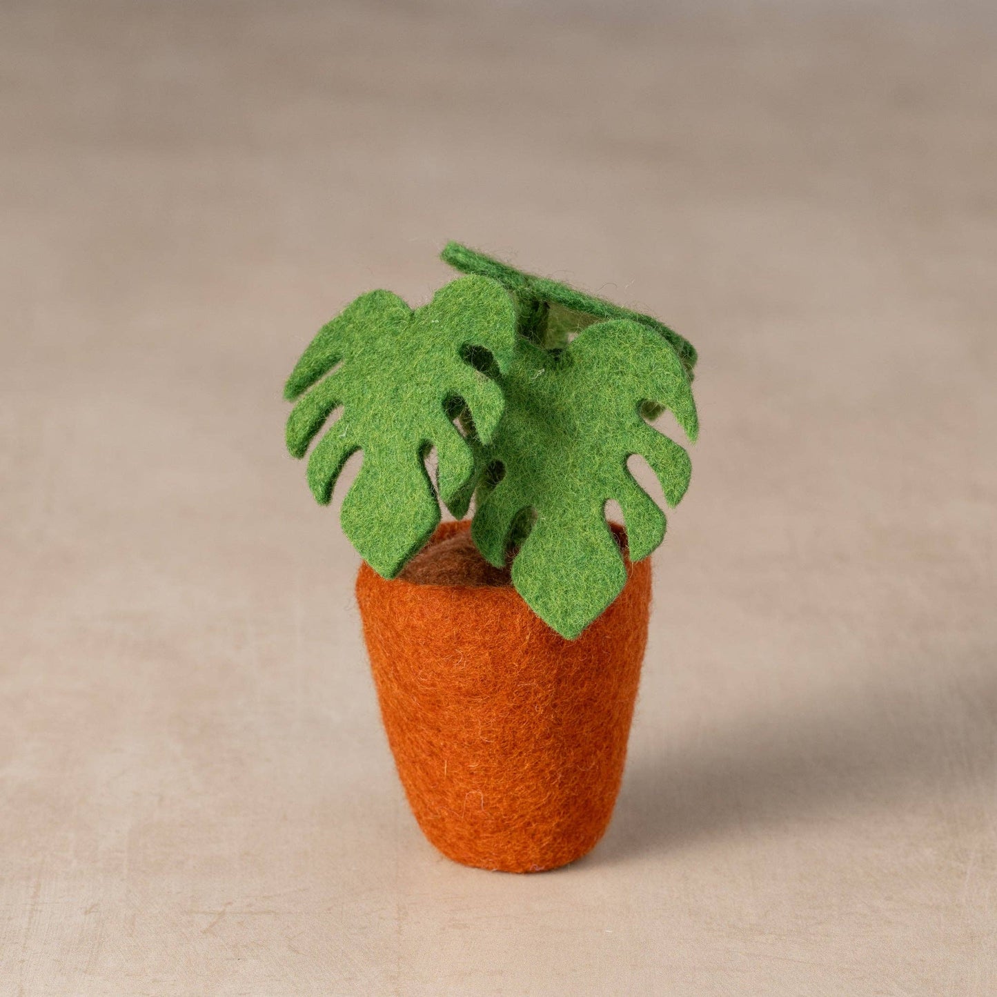 Felted wool Monstera plant in a reddish brown pot with soft green split leaves
