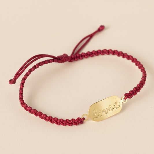 Red braided bracelet with a gold tag on a light gray background