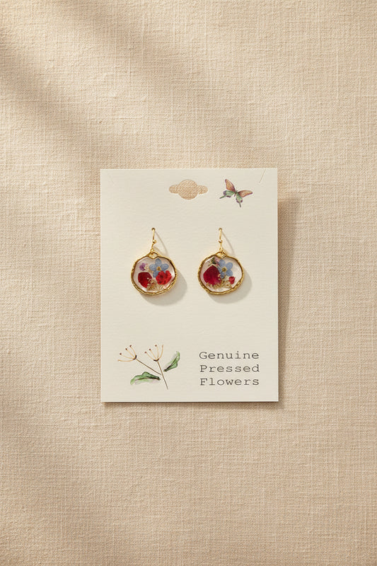 Gold earrings with floral designs on a card labeled 'Genuine Pressed Flowers' against a gray background