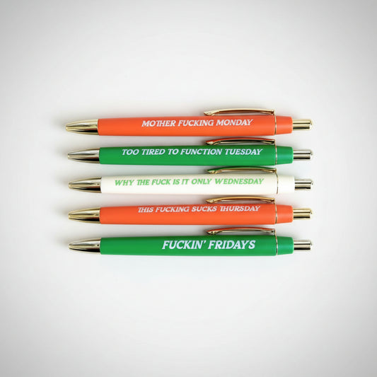 Set of five black ball point pens in red, green, and white colors, with various sayings on them.