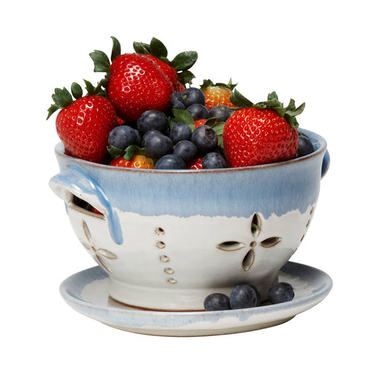 Ceramic colander filled with strawberries and blueberries on a white background