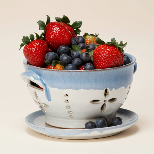 Ceramic colander filled with strawberries and blueberries on a white background