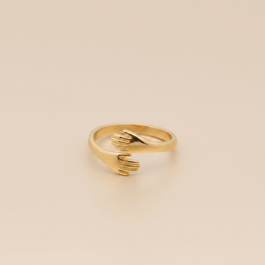 Gold ring shaped like a hand on a textured gray surface