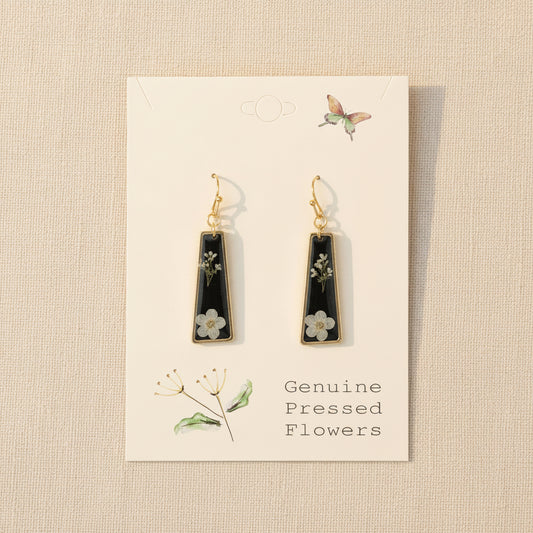 Black teardrop earrings with floral details on a beige card with botanical illustrations.