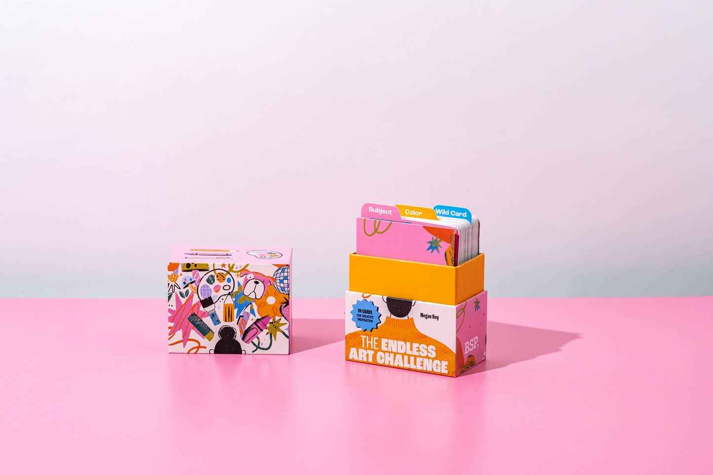 Colorful boxes with art-themed designs on a pink surface