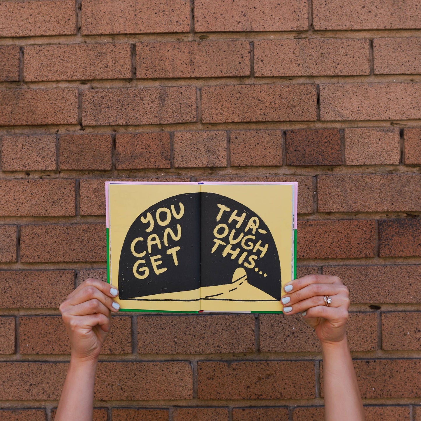 Book with motivational text held up against a brick wall