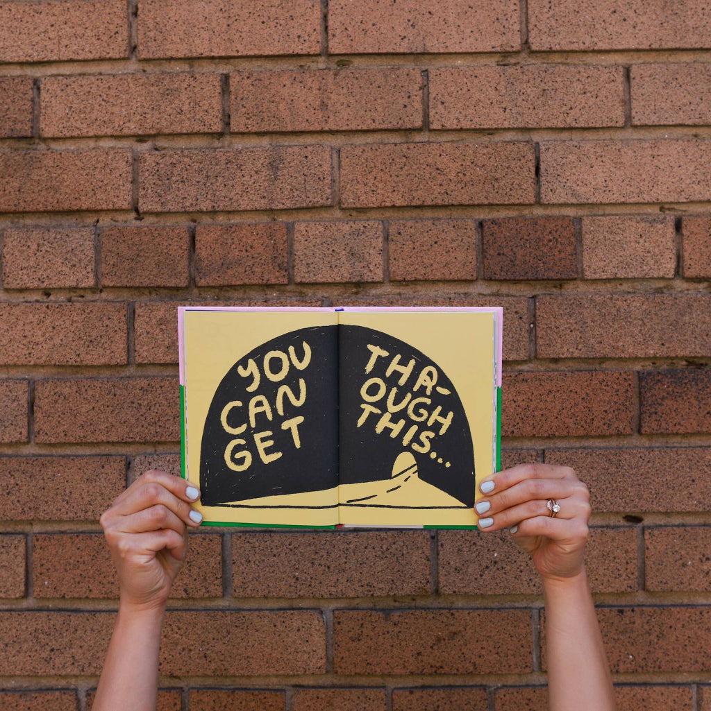 Book with motivational text held up against a brick wall