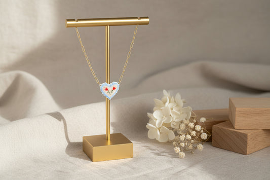 Necklace with a heart-shaped pendant on a gold stand against a neutral background