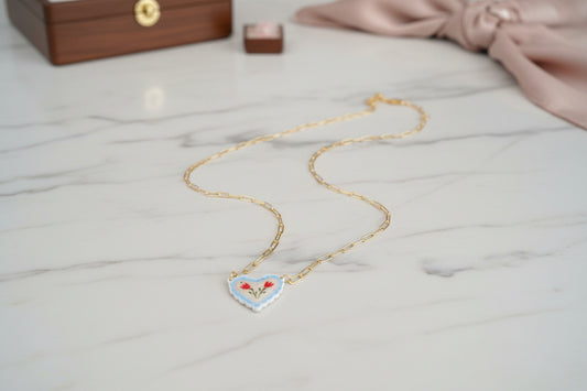 Gold necklace with a heart-shaped pendant on a light gray surface