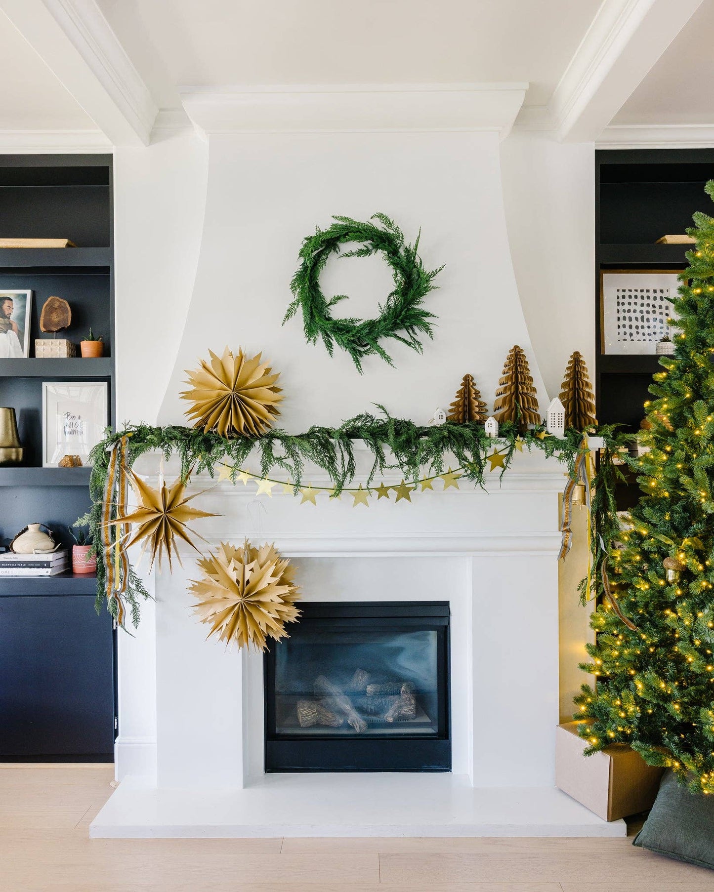 Decorated fireplace with greenery, gold ornaments, and a Christmas tree.