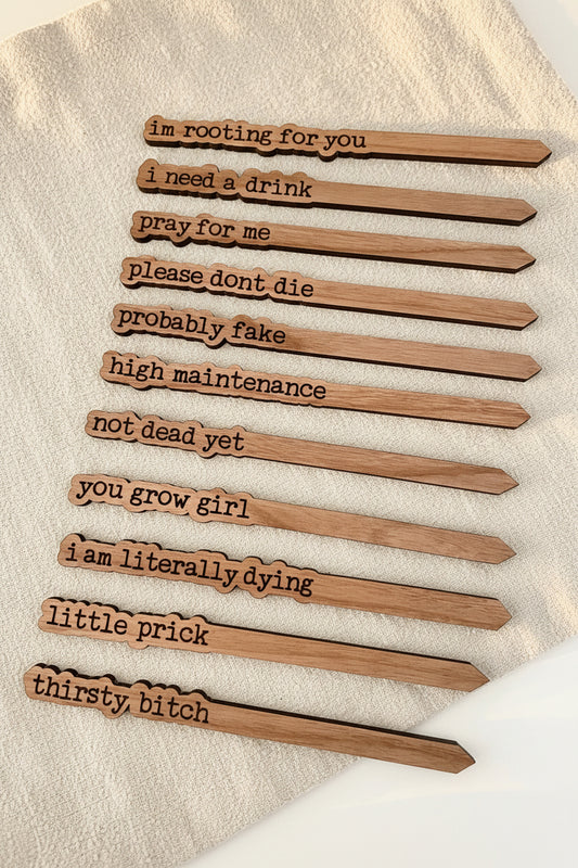 Group of four witty plant stakes including: "Pray for Me," "Thirsty Bitch," "Not Dead Yet," and "You Grow Girl." on a light beige background