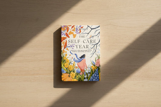 Book titled 'The Self Care Year' with a colorful cover featuring nature-themed illustrations on a white surface.