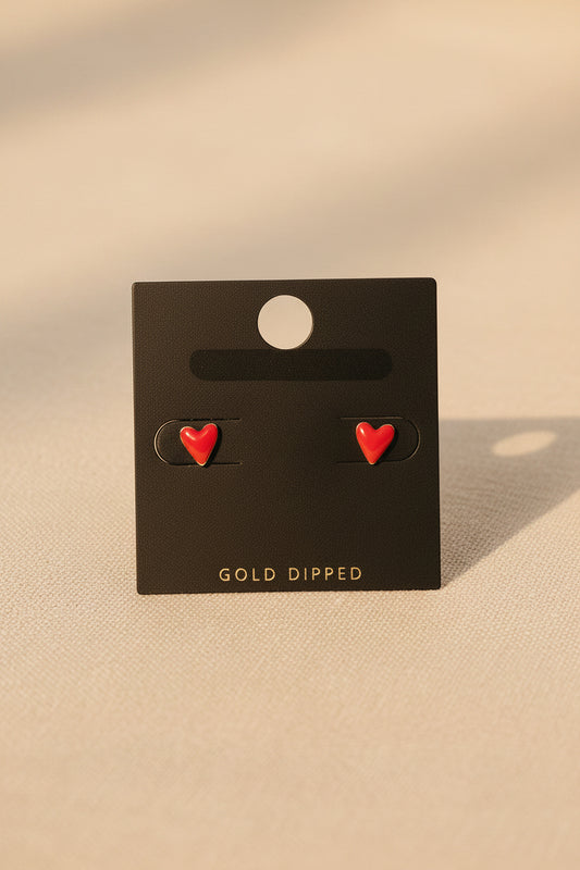 Red heart-shaped earrings on a black card with 'Gold Dipped' text, placed on a beige fabric background.