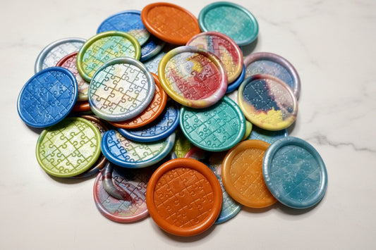 Combination of Autism Awareness wax seal stickers created by Rochambeau Home in various colors and sealed with a puzzle stamp.
