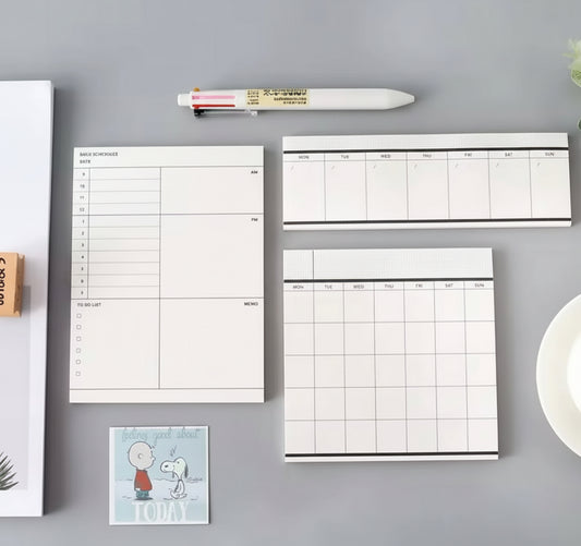 Monochrome monthly weekly daily planner notepads laid out on a desk top.