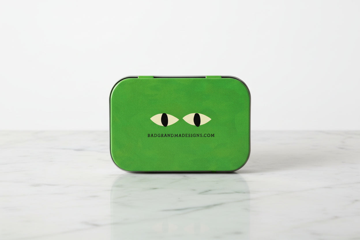 Green rectangular pouch with eye design and 'badgrandmadesigns.com' text on a white background