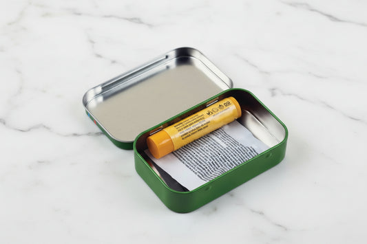 Green metal tin with a yellow chapstick tube and paper inside on a white background