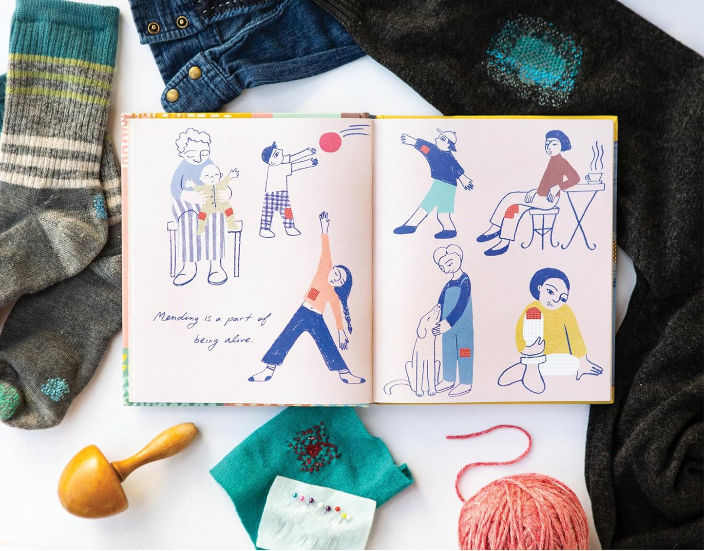 Open book with illustrated pages surrounded by yarn and fabric on a white surface