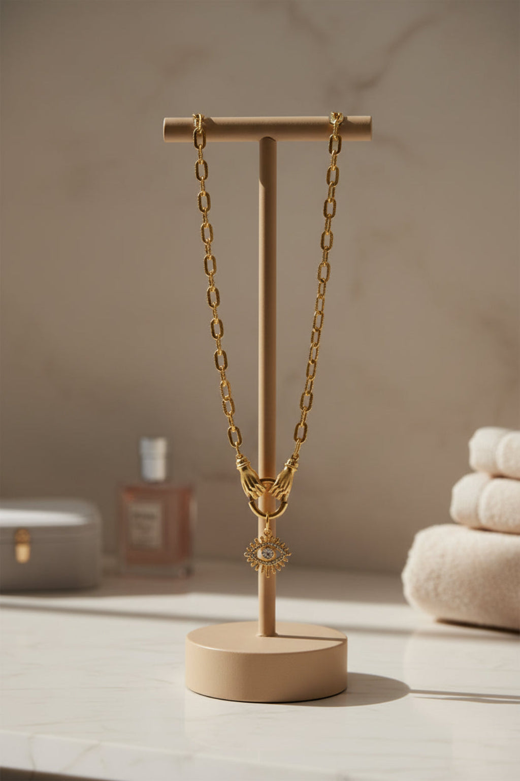 Gold chain necklace with hands holding an evil eye pendant with a bathroom decor background and neutral colors