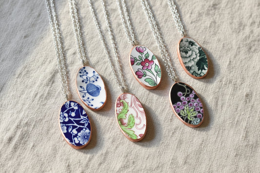 A collection of three oval-shaped necklaces made from recycled china, each featuring a different floral pattern with rose gold trim on a silver chain.