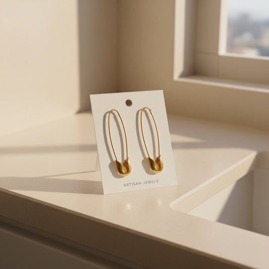 Gold Safety Pin earrings on a white backing card 'Artisan Jewels' propped on a dressing room counter.
