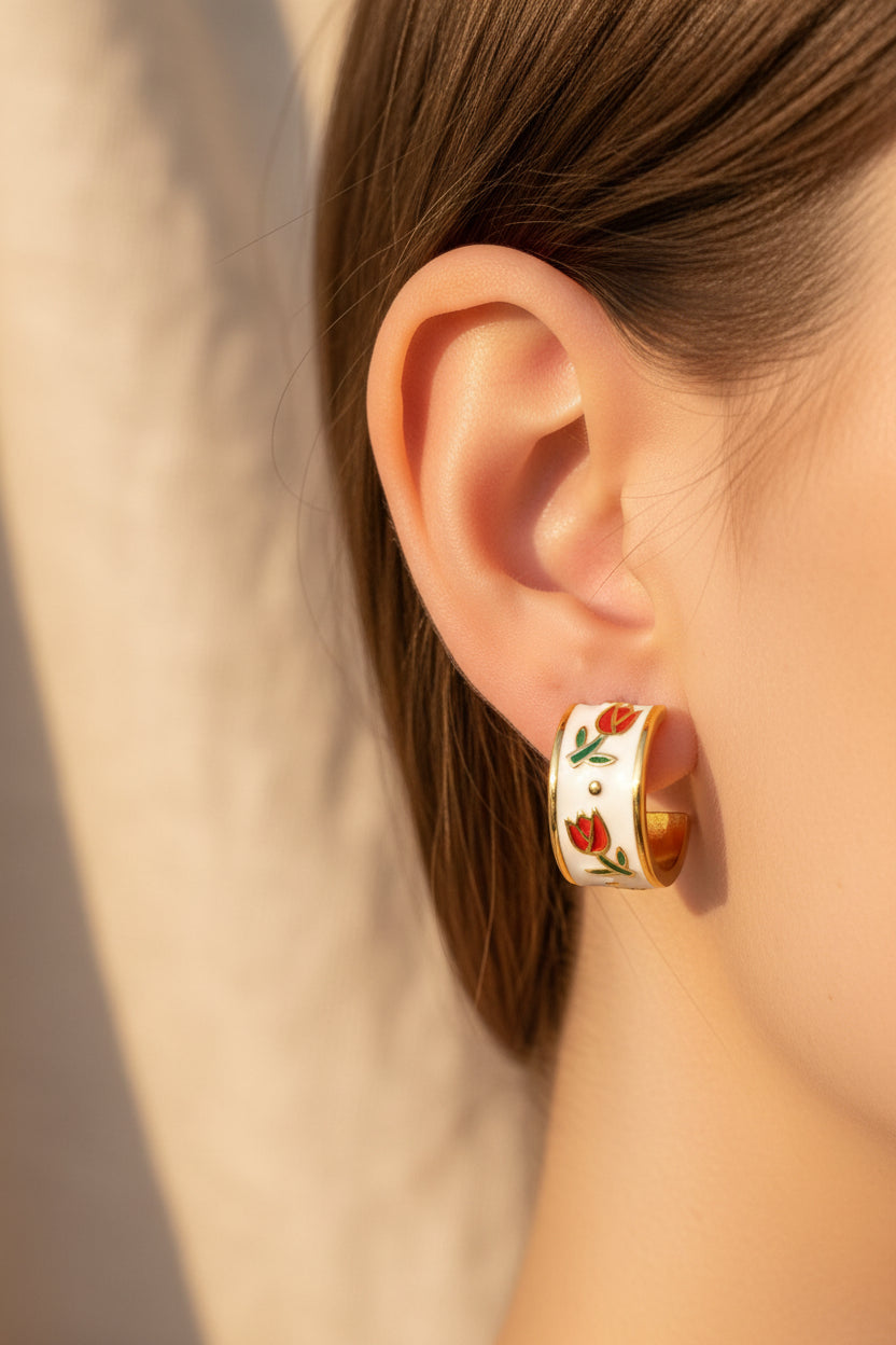 Gold and white earrings with floral design being worn against a beige background