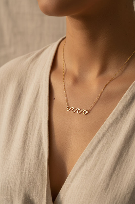 18K gold dipped necklace with 'Crashing Waves' design and worn here with a natural fiber dress and beige background