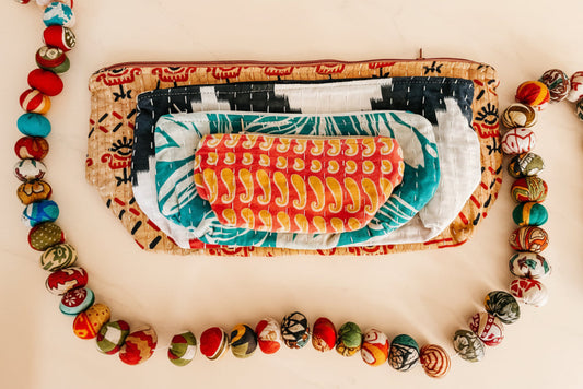 Stack of colorful pouches with patterned contents on a white background and sari garland