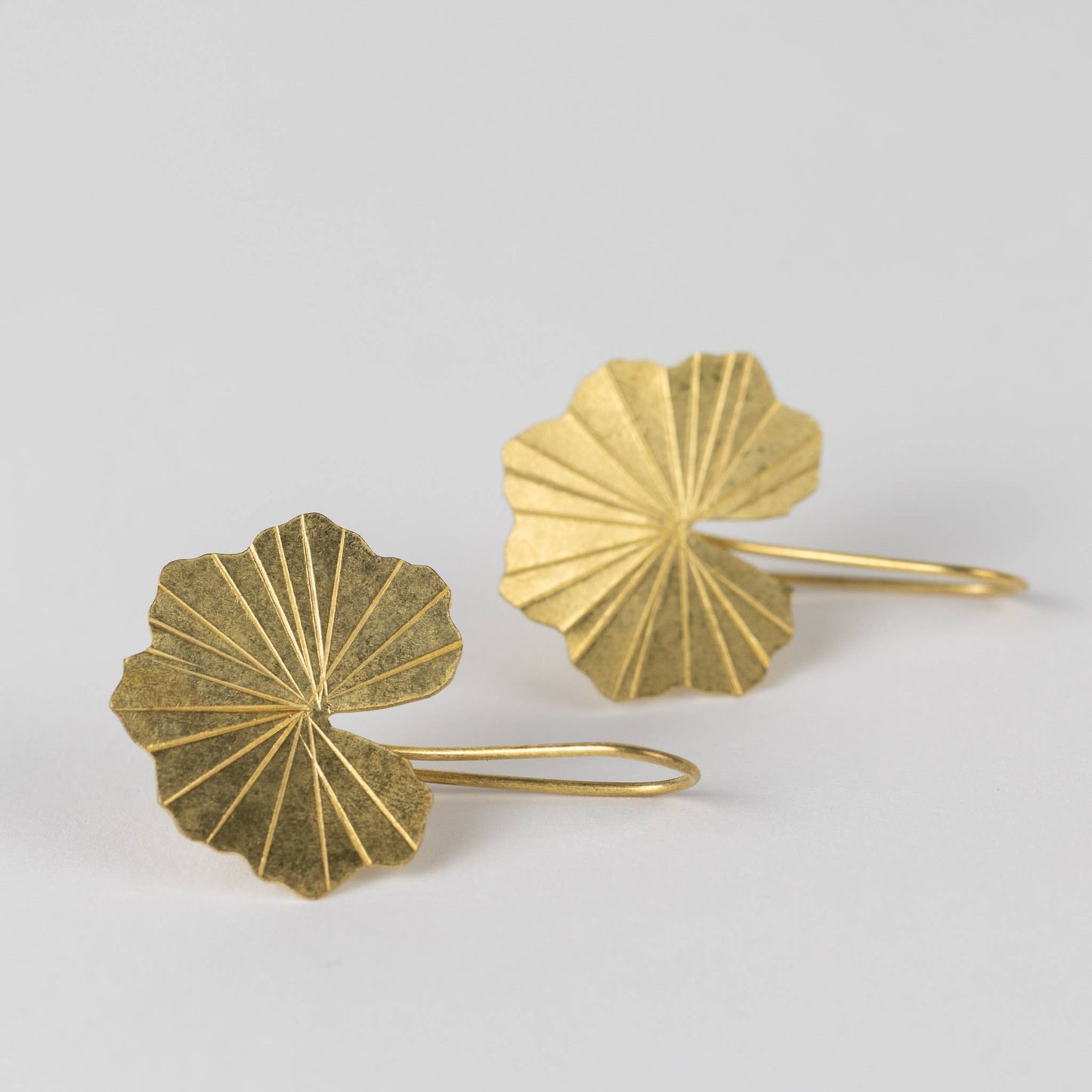 Pair of golden-inspired brass lotus leaf-shaped earrings on a light gray background