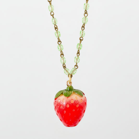 Necklace styled on neutral background with soft shadows emphasizing the glossy red strawberry charm