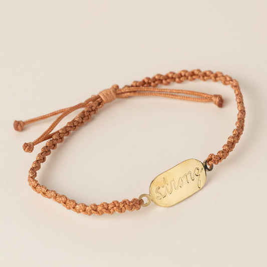 Bracelet with a gold tag and brown cord on a light gray background