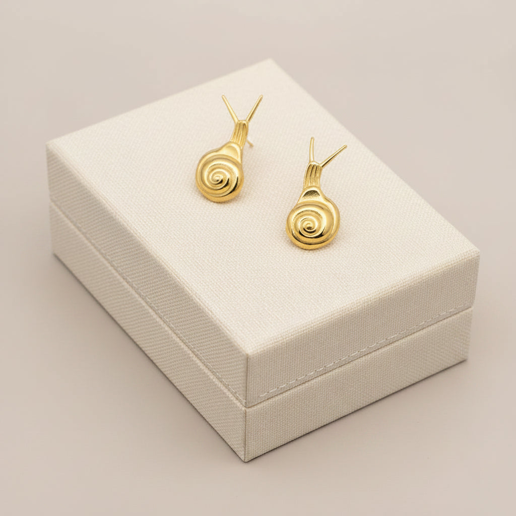 Gold snail-shaped earrings held in a hand against a textured gray background