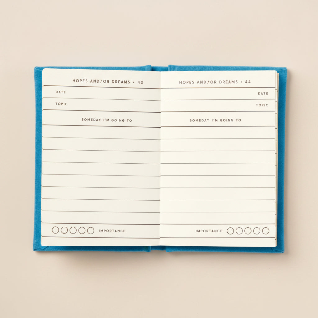 Open mini journal with blue hardcover on a beige background