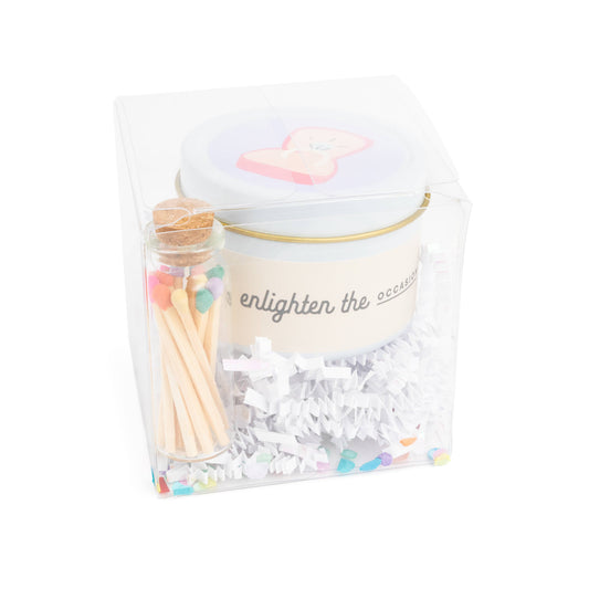 Wedding cake scented candle in white tin with corked vial of colorful matchsticks, packaged in a clear vinyl gift box.