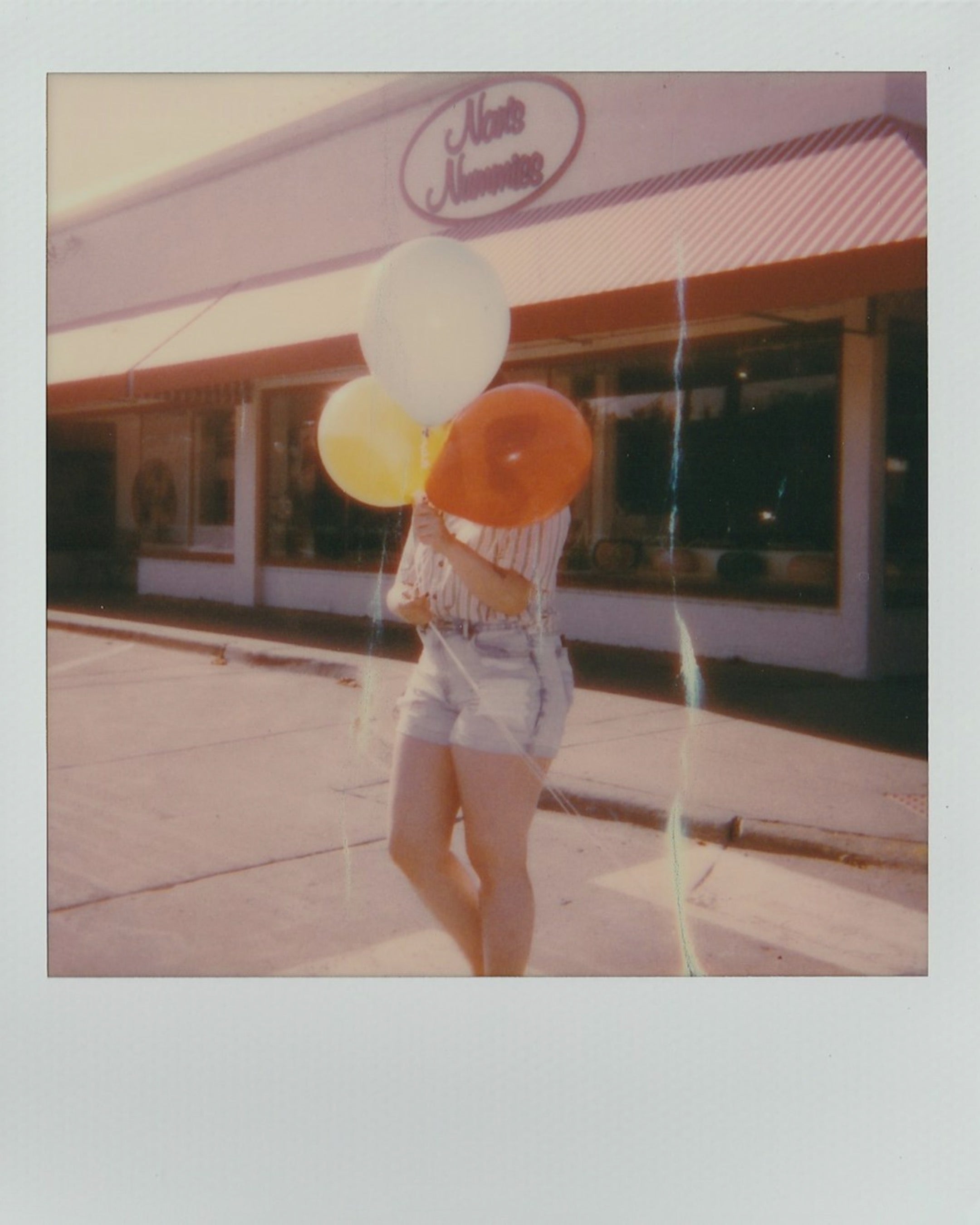 Polaroid picture of a person holding balloons to cover her face in a vintage image