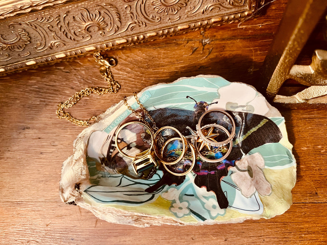 A handcrafted oyster shell trinket dish with floral and butterfly collage, gold accents, and glossy finish, perfect for holding jewelry. Created by Rochambeau Home