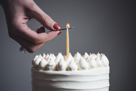 A person's hand lighting a single candle on a white decorated birthday cake.