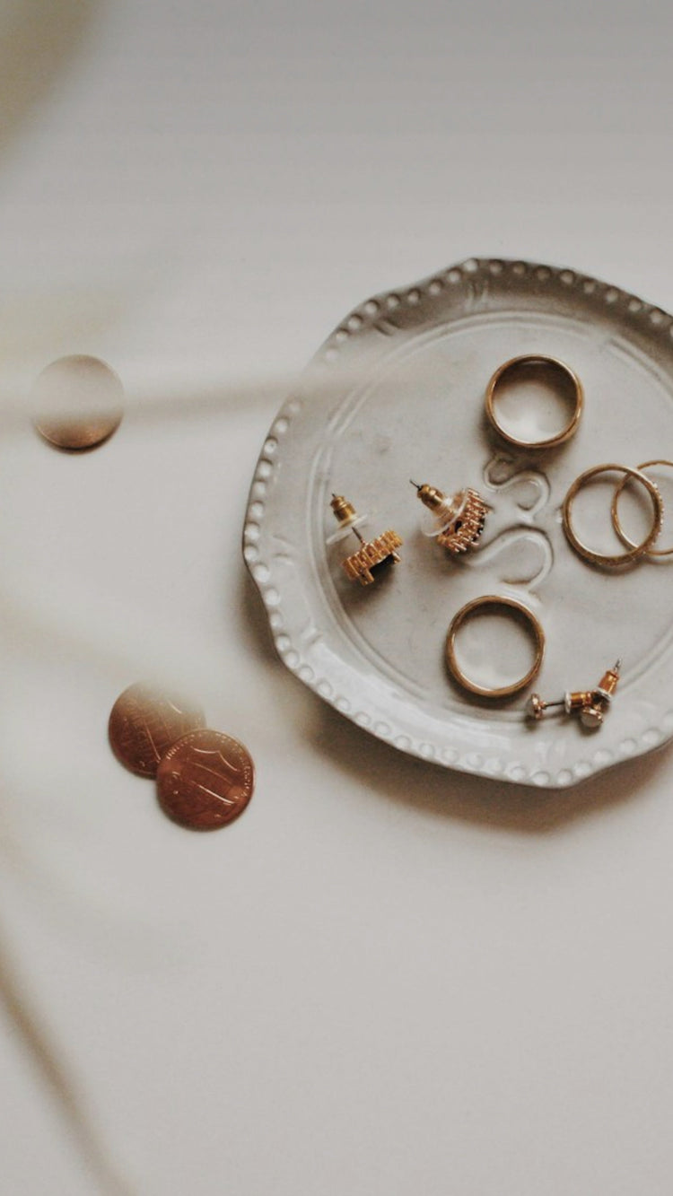 Image of jewelry pieces laying on a trinket dish with a white background