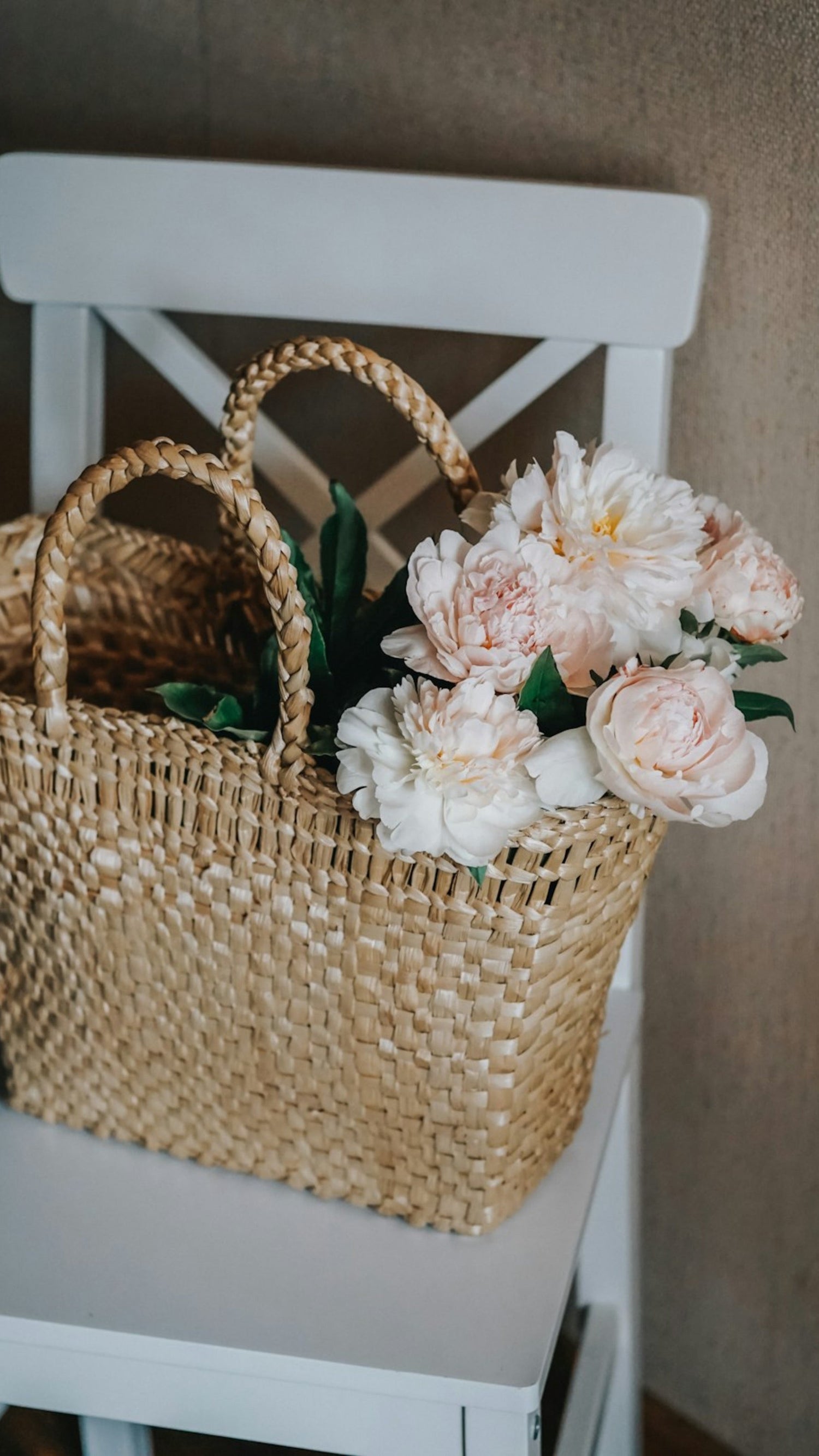 Image of a basket weaved bag carrying several pale blush pink peonies 