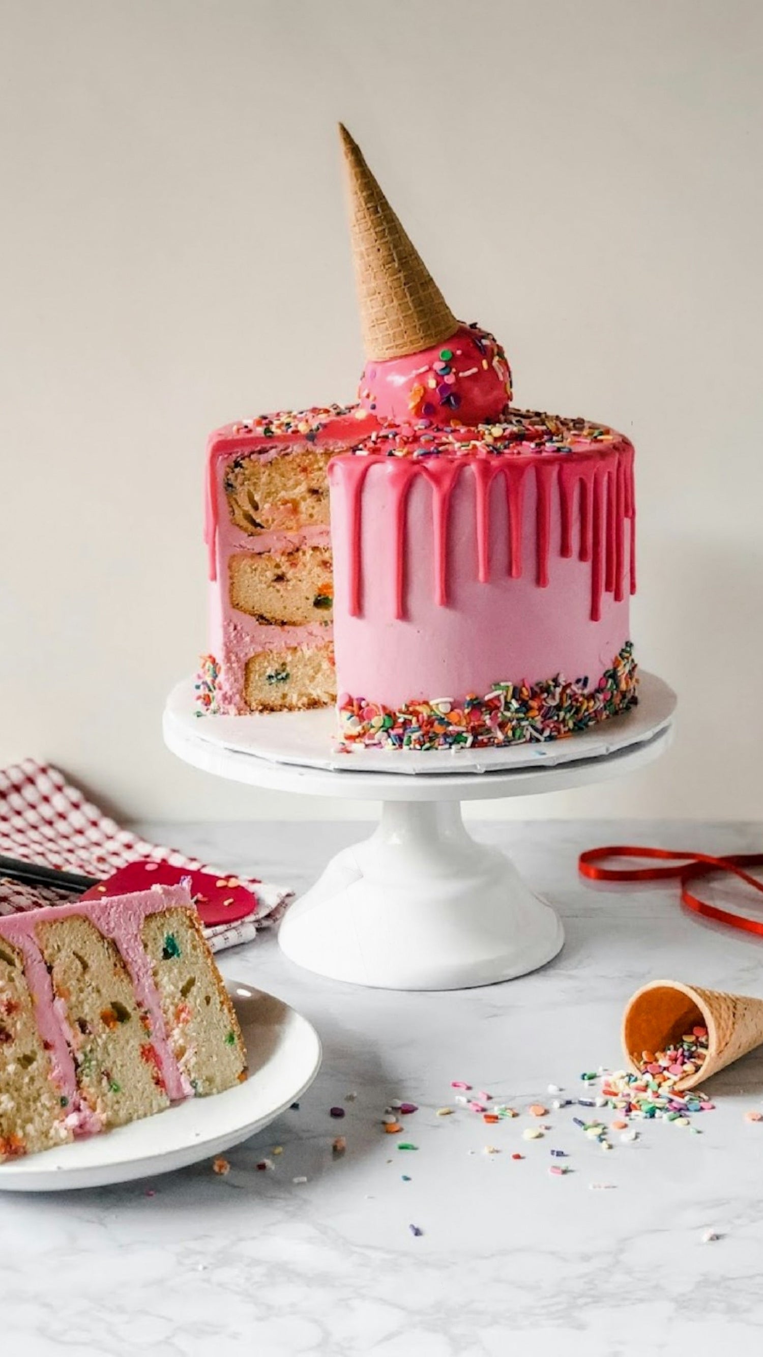 Image of a pink cake with sprinkles and other birthday elements on a beige background