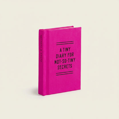 Mini pink diary with text, "A Tiny Diary for Not-So-Tiny Secrets" on a light beige ackground