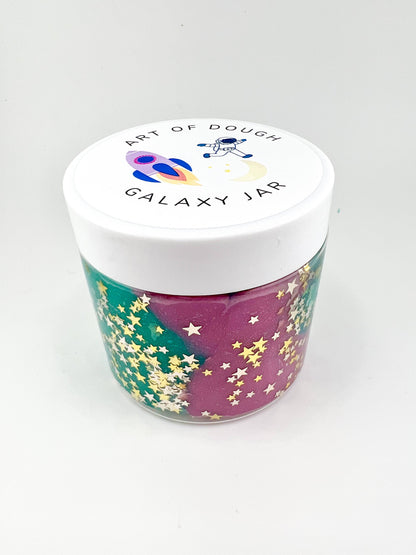 A 6oz jar with star-glitter sensory dough, a rocket ship cutter, a space figurine, and assorted gems for sensory engagement.