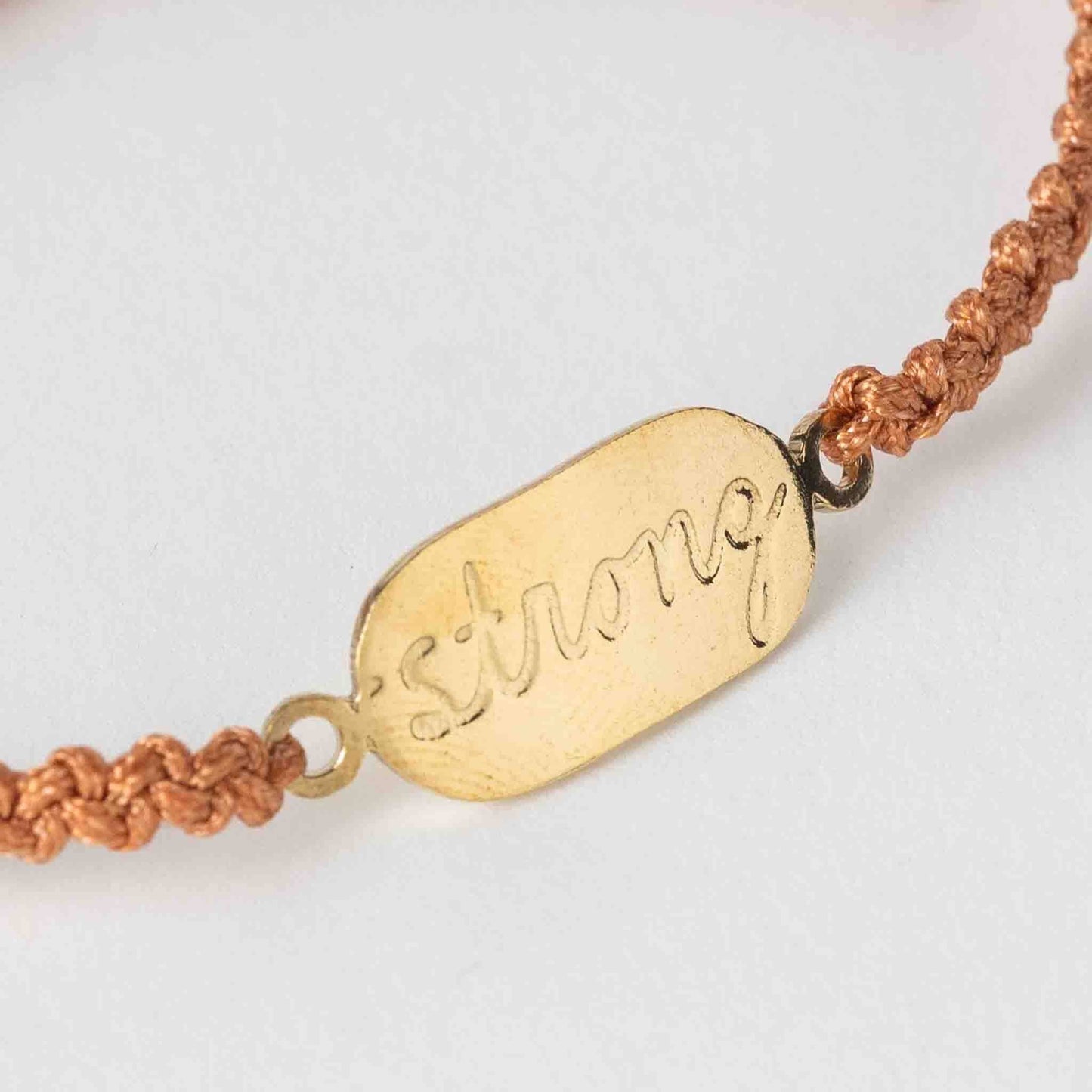 Bracelet with gold tag that says 'strong' on a white background